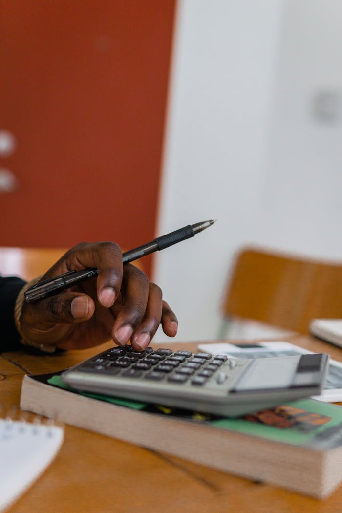 Close-up shot of a hand holding a pen while calculating finances with a calculator on a table.