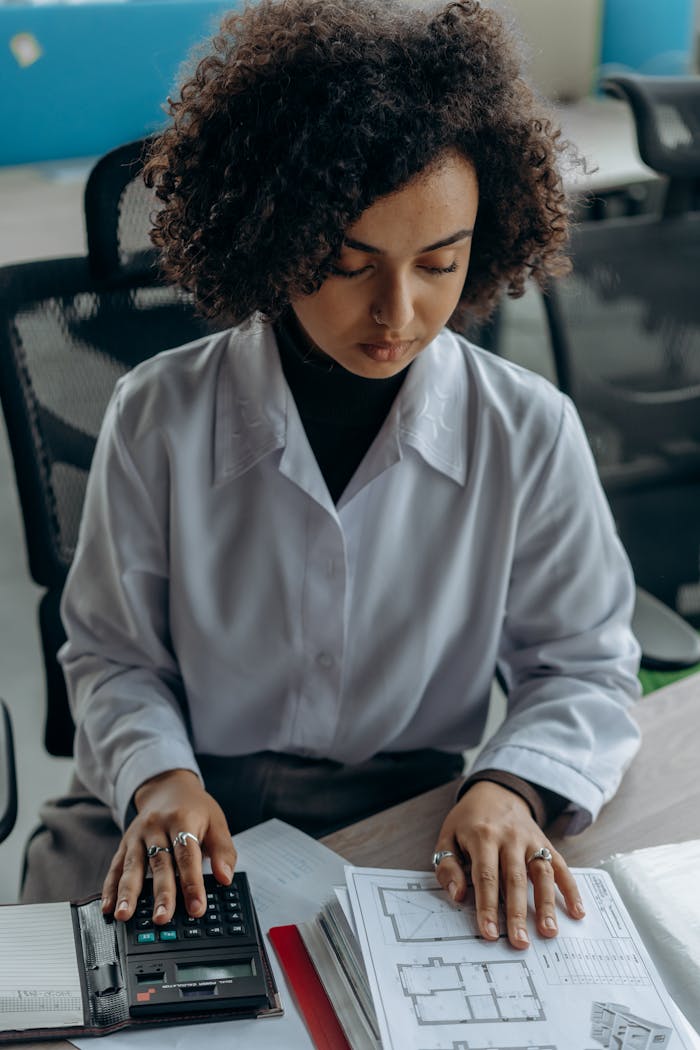 Businesswoman calculating finances at her desk with documents and a calculator.